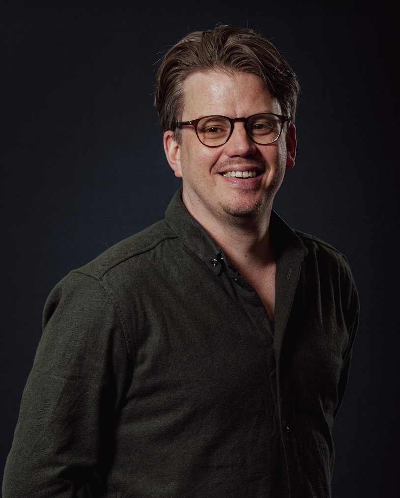 Portret van Jerre Maas, lachend, in een donkergroen overhemd