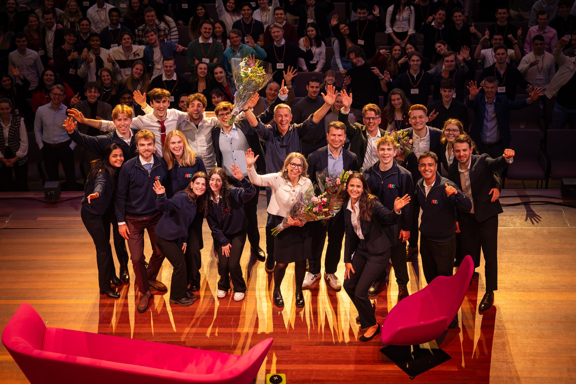 Groepsfoto op het podium voor een volle zaal bij symposium The Road