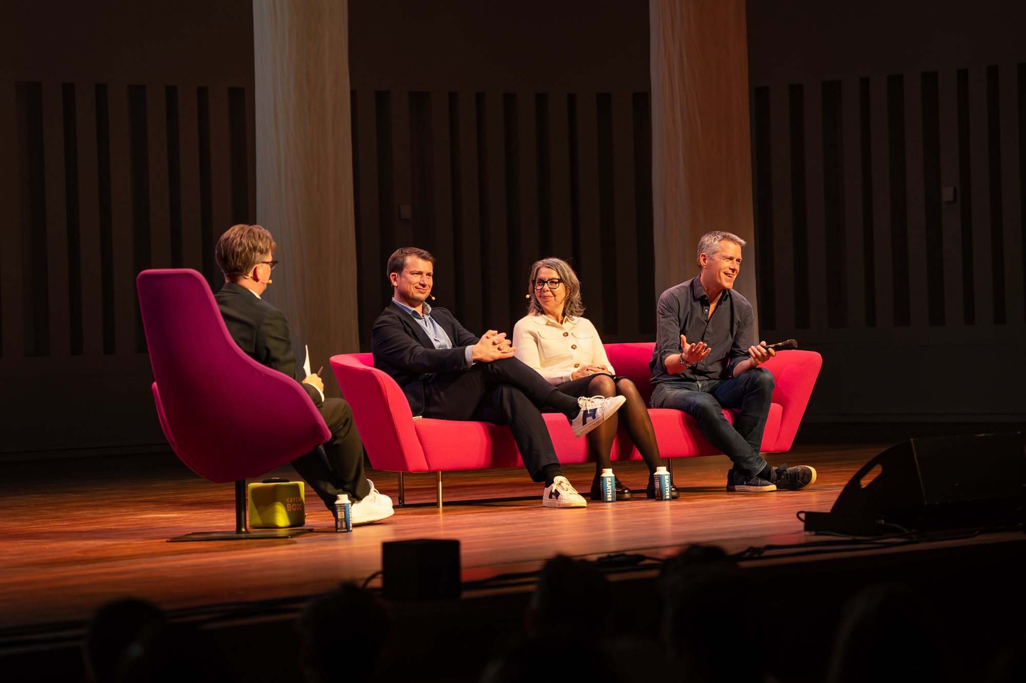 Jerre Maas modereert een panelgesprek met drie gasten op een roze bank tijdens The Road Symposium