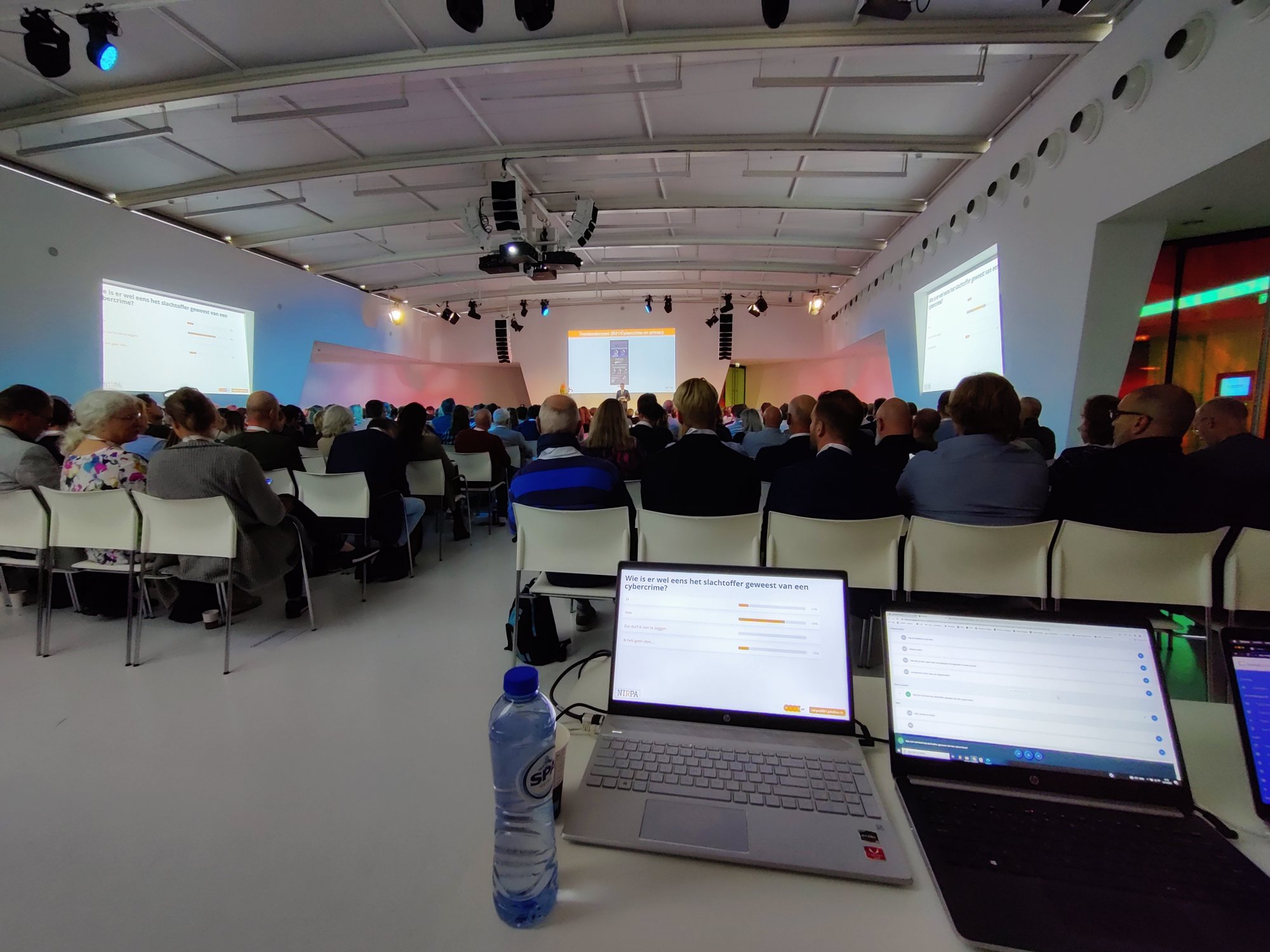 Volle congreszaal waar de resultaten van een live poll via PresentersWall op de schermen en laptops staan