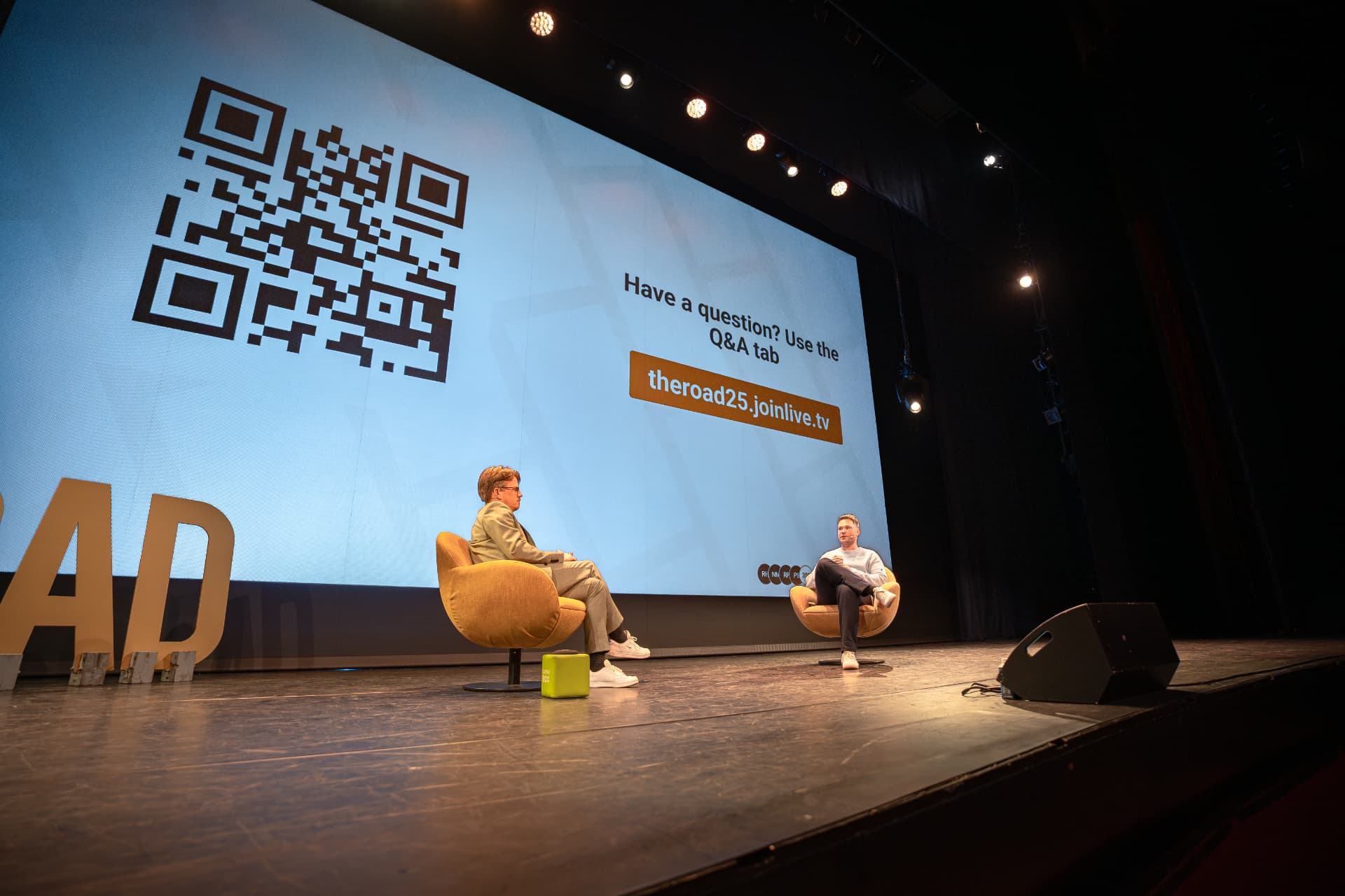 Grote QR-code op het scherm waarmee de zaal vragen kan stellen, met Jerre Maas in gesprek op het podium