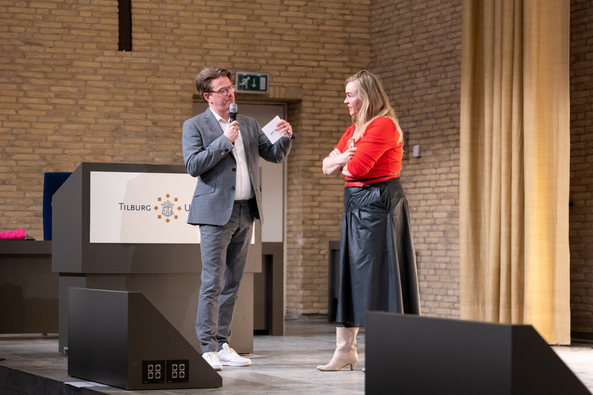 Jerre Maas presenteert met een co-presentator naast het spreekgestoelte van Tilburg University